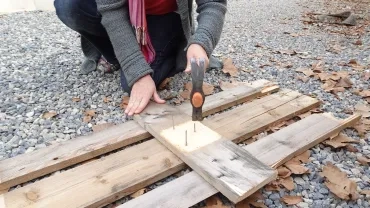 une personne enlève les clous d'une palette grâce à un marteau
