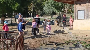 un groupe d'enfants et leurs animateur tiennent un tuyau d'arrosage et versent de l'eau dans une mare