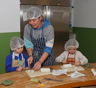 deux enfant et leur animatrice coupent des bûches de chèvre
