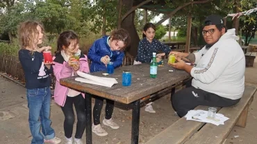 un groupe d'enfants et leur animateur montrent des bocaux remplis de couleurs et de paillettes