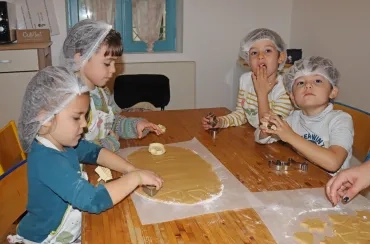 un goupe d'enfants en cuisine posent des emporte-pièces sur une pâte