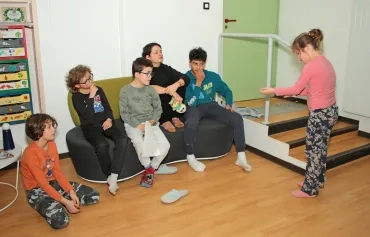 un groupe d'enfants et leur animatrice sont assis sur un banc et regarde une enfant en traint de faire des gestes