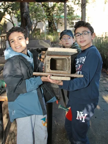 trois enfants montrent une petite cabane en bois