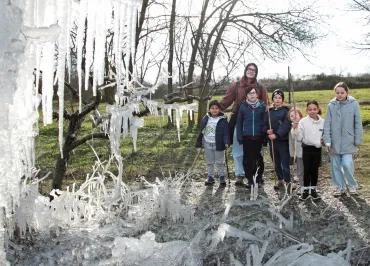 un groupe d'enfants et leur animateur posent derrière une sculpture de glace avec des stalagtites et des stalagmites