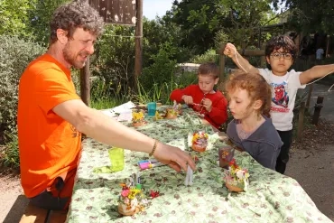 Un groupe d'enfants et leur animateur collent des fleurs sur des pots en terre