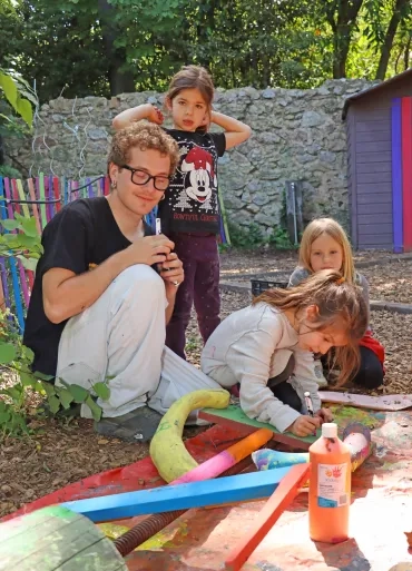 Un groupe d'enfants et leur animateur peignent des morceaux de bois