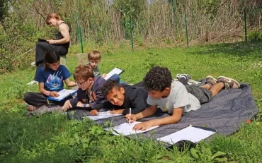 Un groupe d'enfants et leur animateur sont allongés dans l'herbe en train de dessiner