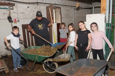 Un groupe d'enfants et leur animateur sont dans la rgange avec des brouettes et des pelles