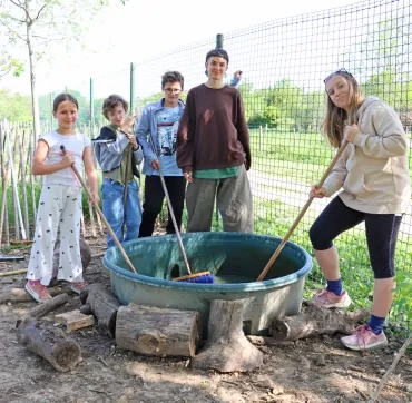 Un groupe d'enfants et leur animatrice frottent une bassine avec des balai 