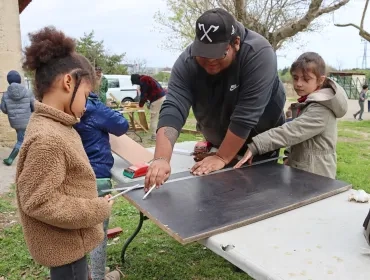 Deux enfants et leur animateur prennent des mesures sur une planche en bois