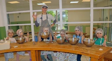 Un groupe d'enfants et leur animatrice sont en cuisine avec des saladiers et des fouets