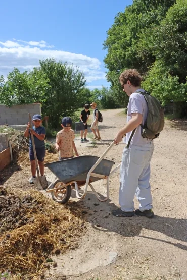 une groupe d'enfants et leur animateur vident une brouette à l'aire de compostage