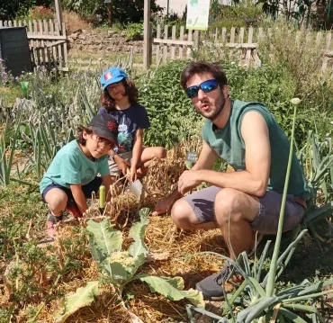 deux enfants et leur animateur cueillent de l'ail au jardin