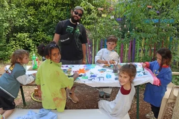 Un groupe d'enfants et leur animateur peignent sur un drap