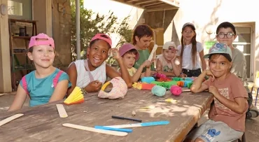 un groupe d'enfants et leur animatrice plient des feuilles de papier colorées