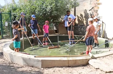 un groupe d'enfants et leur animateur frottent la mare avec des balais