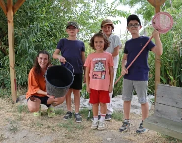 un groupe d'enfants et leur animatrice sont devant une mare avec un seau et une épuisette