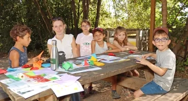 un groupe d'enfants et leur animatrice plient du papier