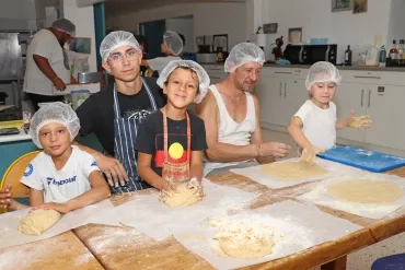 un groupe d'enfants et leurs animateurs étalent de la pâte en cuisine
