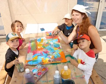 un groupe d'enfants et leur animatrice peignent sur une grande feuille