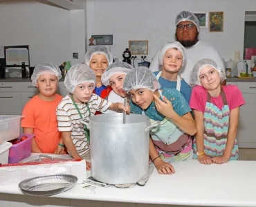 un groupe d'enfants et leur animateur posent avec une grande marmite en cuisine