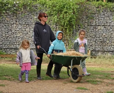Un groupe d'enfants et leur animatrice poussent une brouette pleine de paille