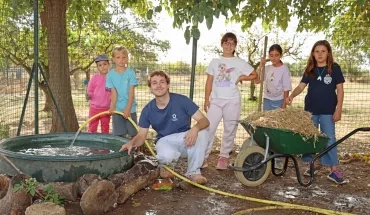 Un groupe d'enfants et leur animateur sont autour d'une bassine avec une brouette de paille