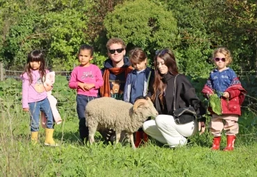Un groupe d'enfants et leurs animateurs caressent un bélier blanc