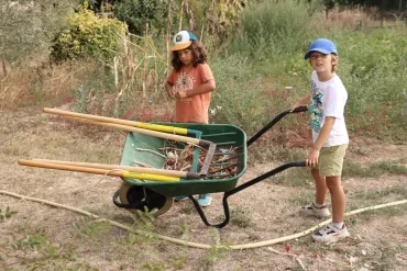 Deux enfants posent avec une brouettes avec eds oignons à l'intérieur et un outil de jardin