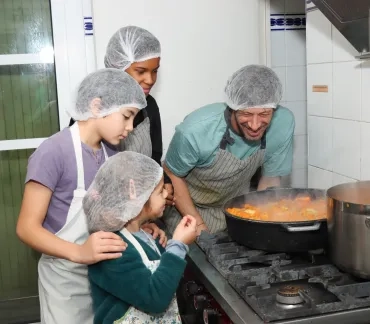Un groupe d'enfants et leur animateur sont en cuisine autour d'une grosse marmite de soupe