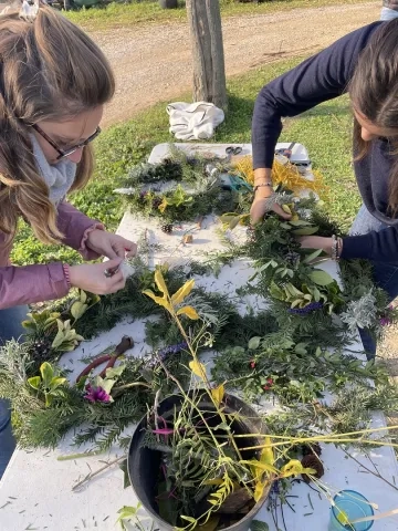 Deux adultes créent une couronne de feuille, il y a différentes feuilles, branches et fleurs